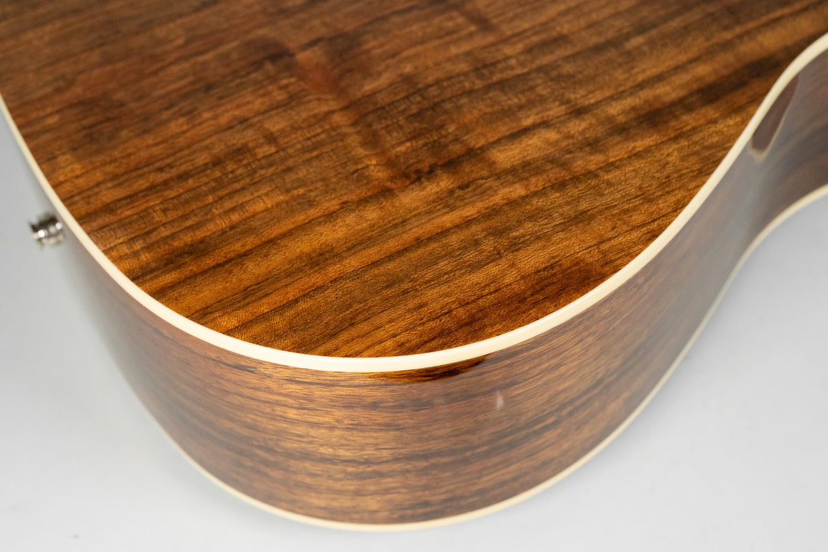 Close-up of the guitar's lower bout, showing the dark brown, figured wood grain of the top and side, with light binding.