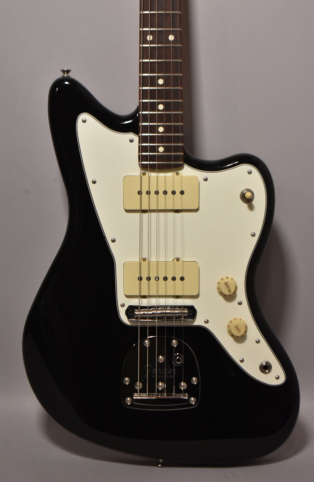 A black Jazzmaster guitar with a white pickguard, two cream P90 pickups, and chrome hardware, viewed from the front.