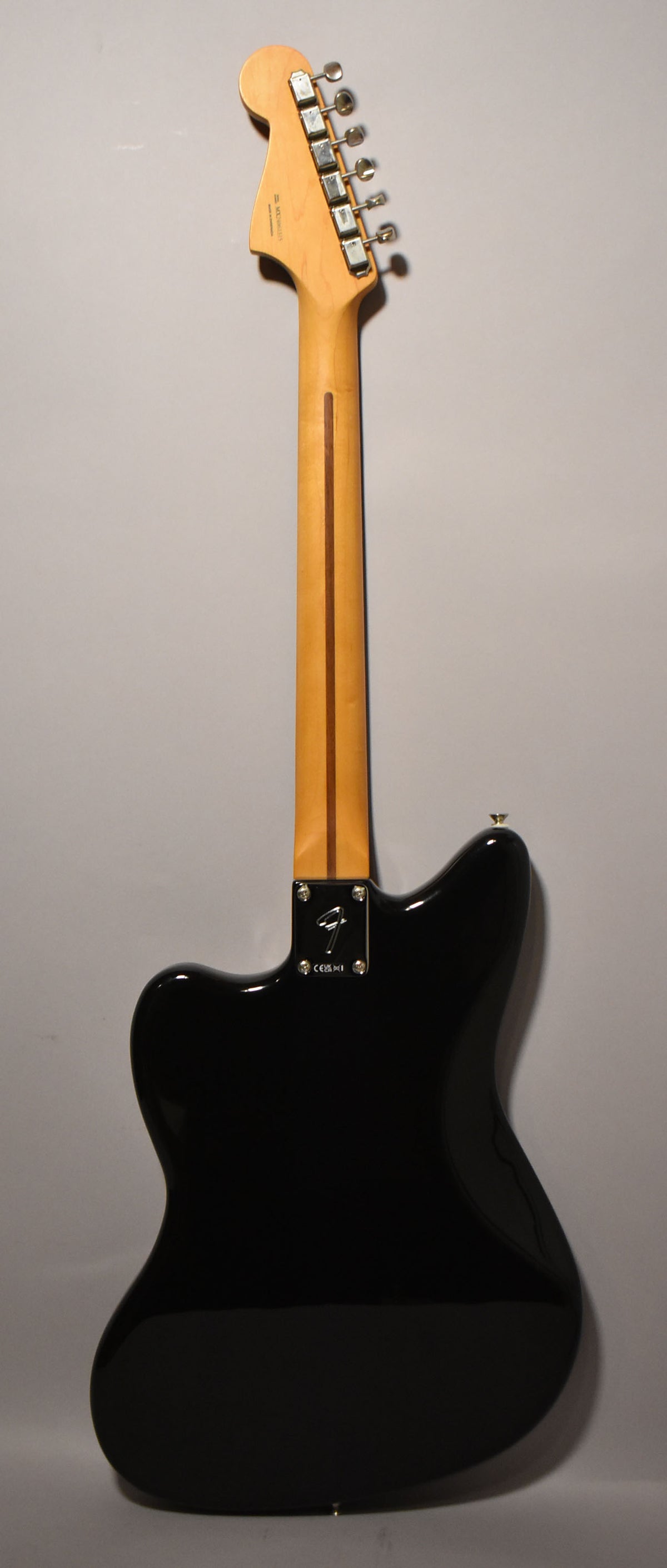 Full rear view of a black Jazzmaster with a glossy finish, showing the light maple neck, headstock with six chrome tuners, and a chrome neck plate.