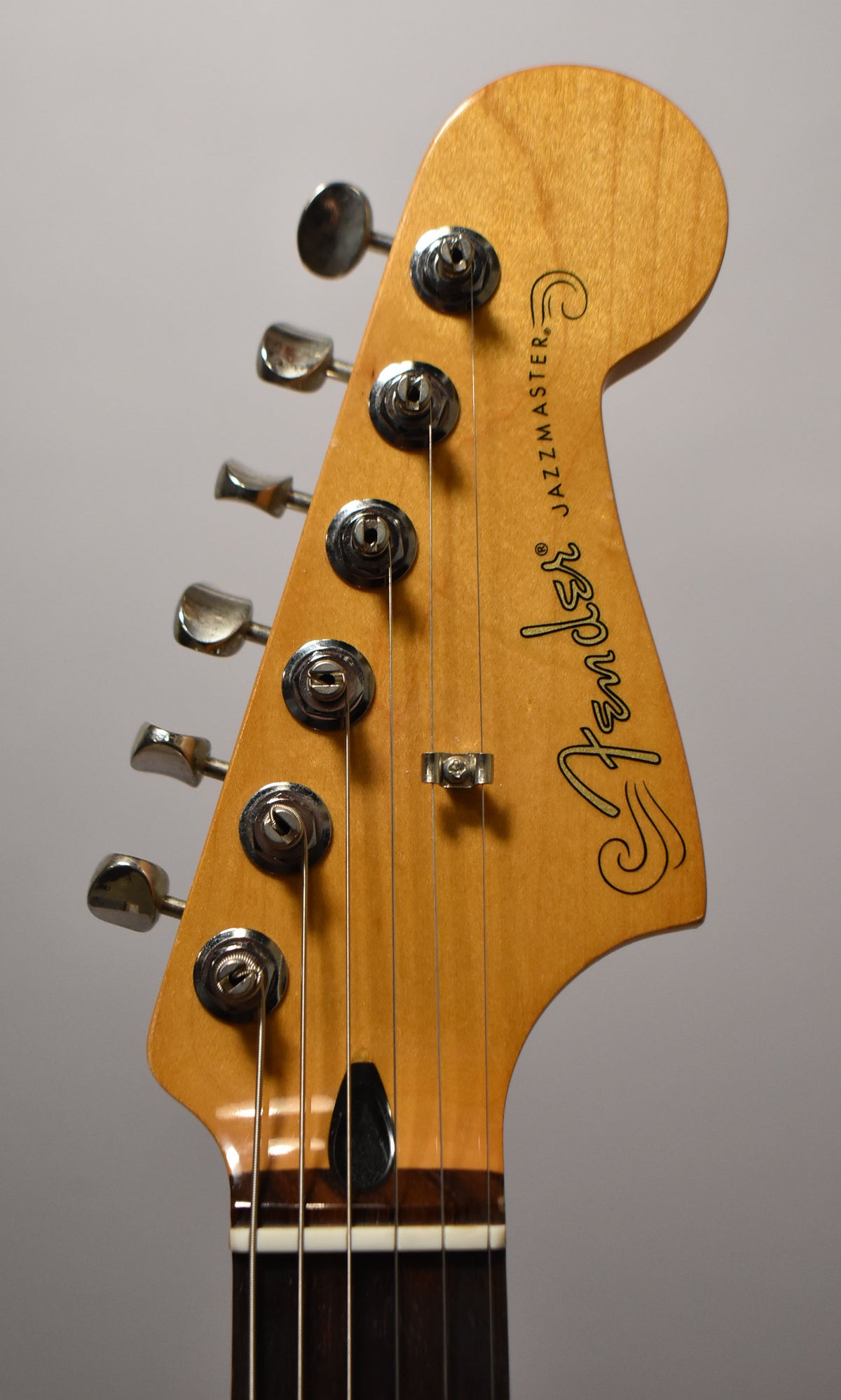 Close-up of the guitar's headstock, angled slightly left, showing six chrome tuners, a string tree, and a dark truss rod cover.
