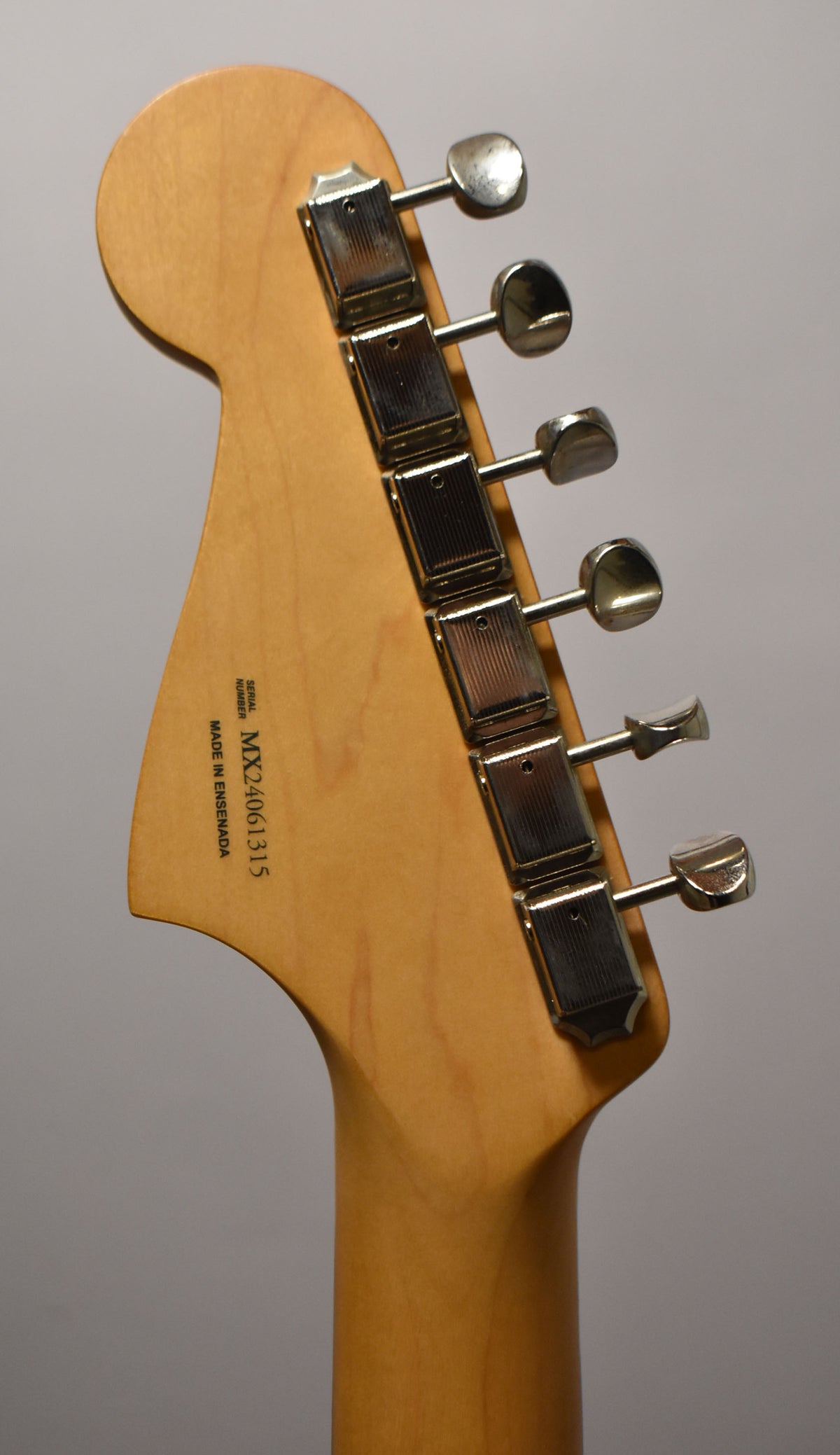 Rear view of the natural wood headstock and neck, showing six chrome tuning machines and the serial number.