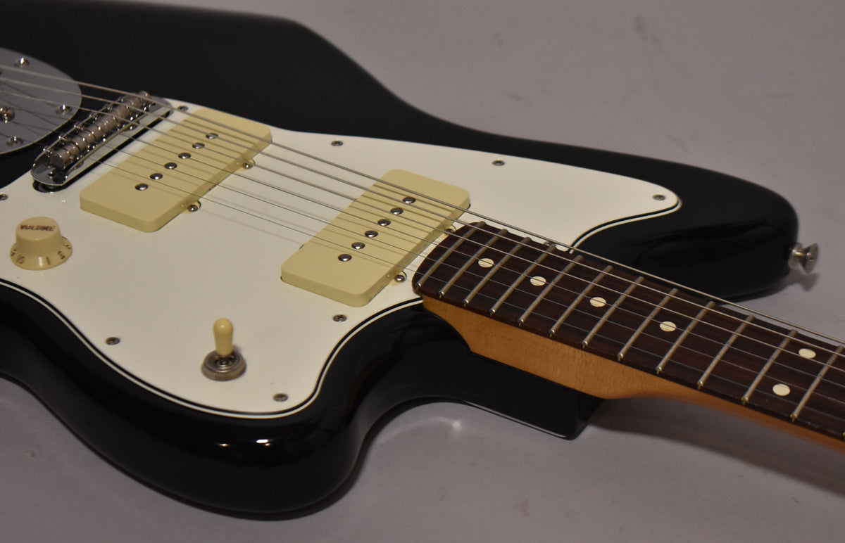 Close-up of a glossy black guitar body with a white pickguard, cream P90-style pickups, and a maple neck with a dark fretboard.