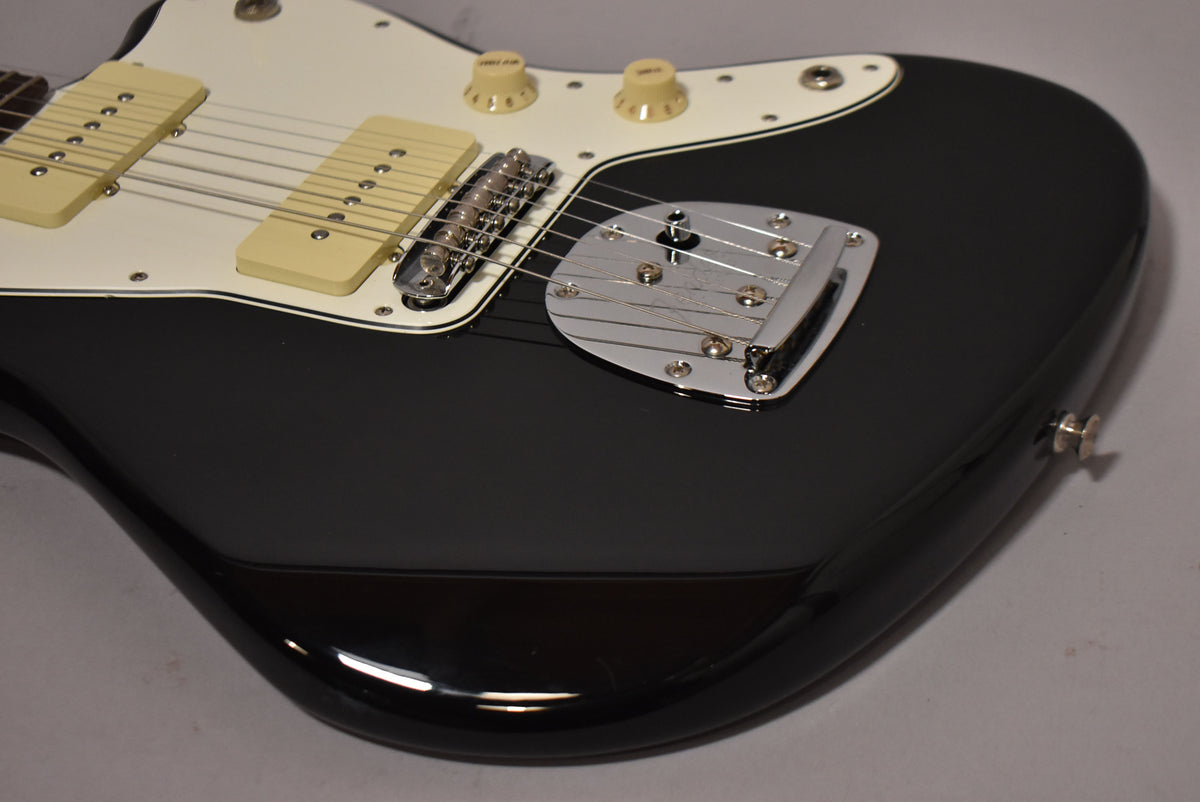 Close-up of the glossy black body and white pickguard, showing cream pickups, chrome bridge, and vibrato tailpiece.
