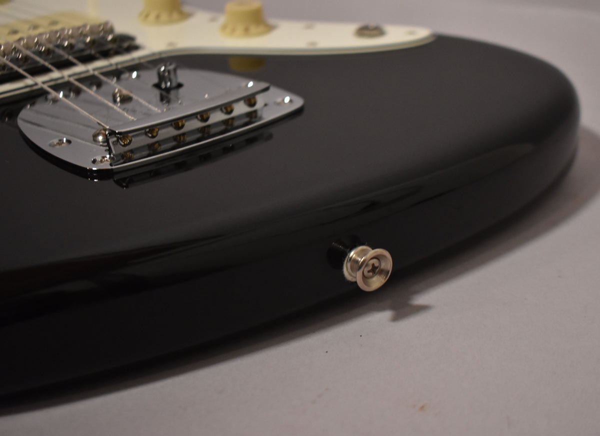Close-up of the glossy black Jazzmaster body, showing the chrome bridge, cream pickguard, and the strap button on the lower bout.