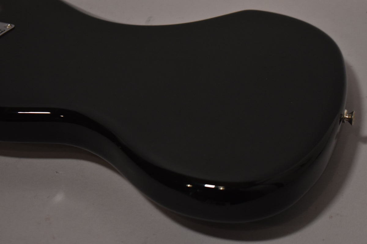 The lower bout of a black gloss Jazzmaster body is angled, showing the smooth finish and a chrome strap button on the bottom edge.