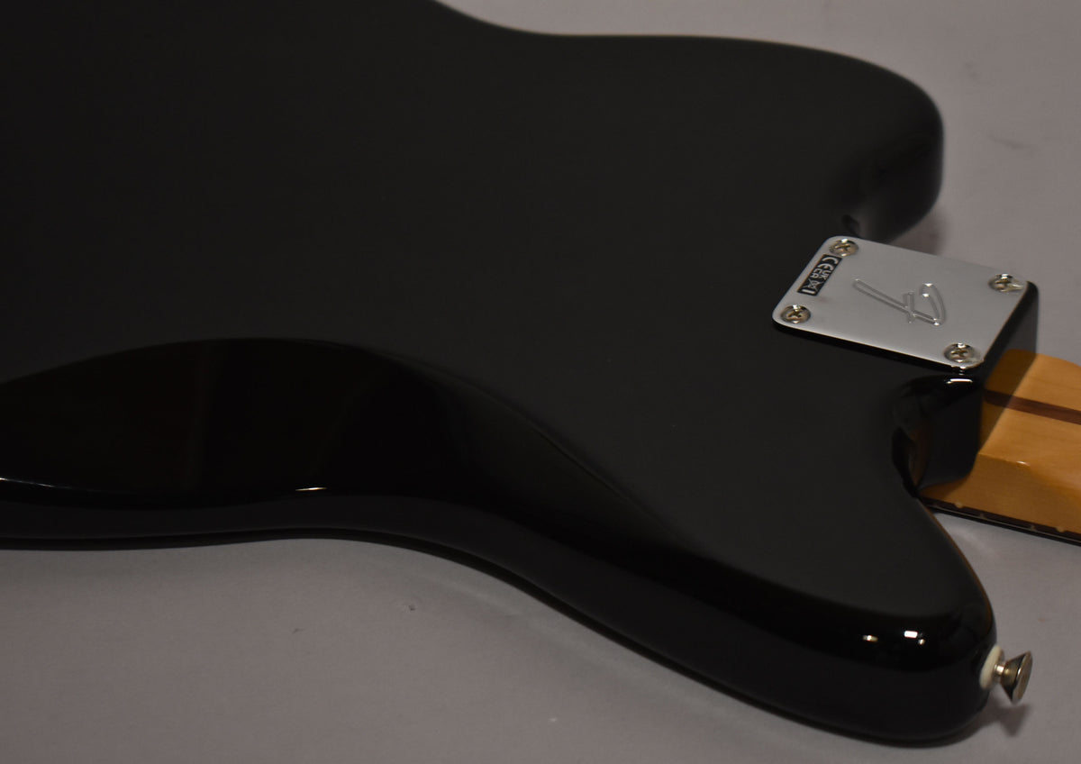 The guitar's glossy black body is seen from the back, angled to show the chrome neck plate and a strap button at the bottom.