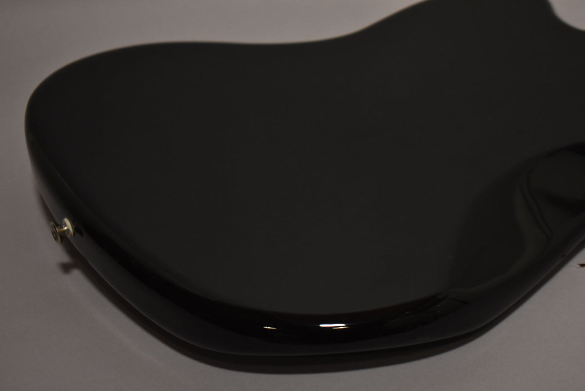 Close-up of the guitar's glossy black body from the upper bout, showing the strap button and a slight reflection along the lower edge.