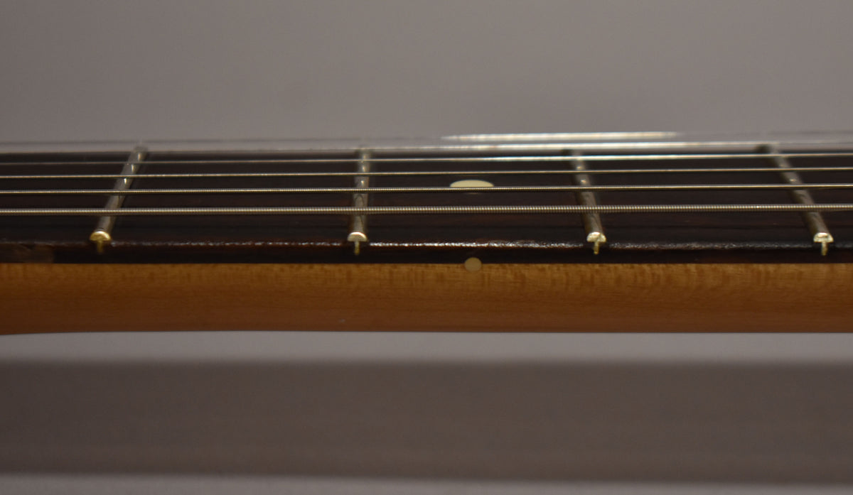 A close-up of the guitar's fretboard and neck, showing the dark wood fretboard with light fret markers and a light wood neck.