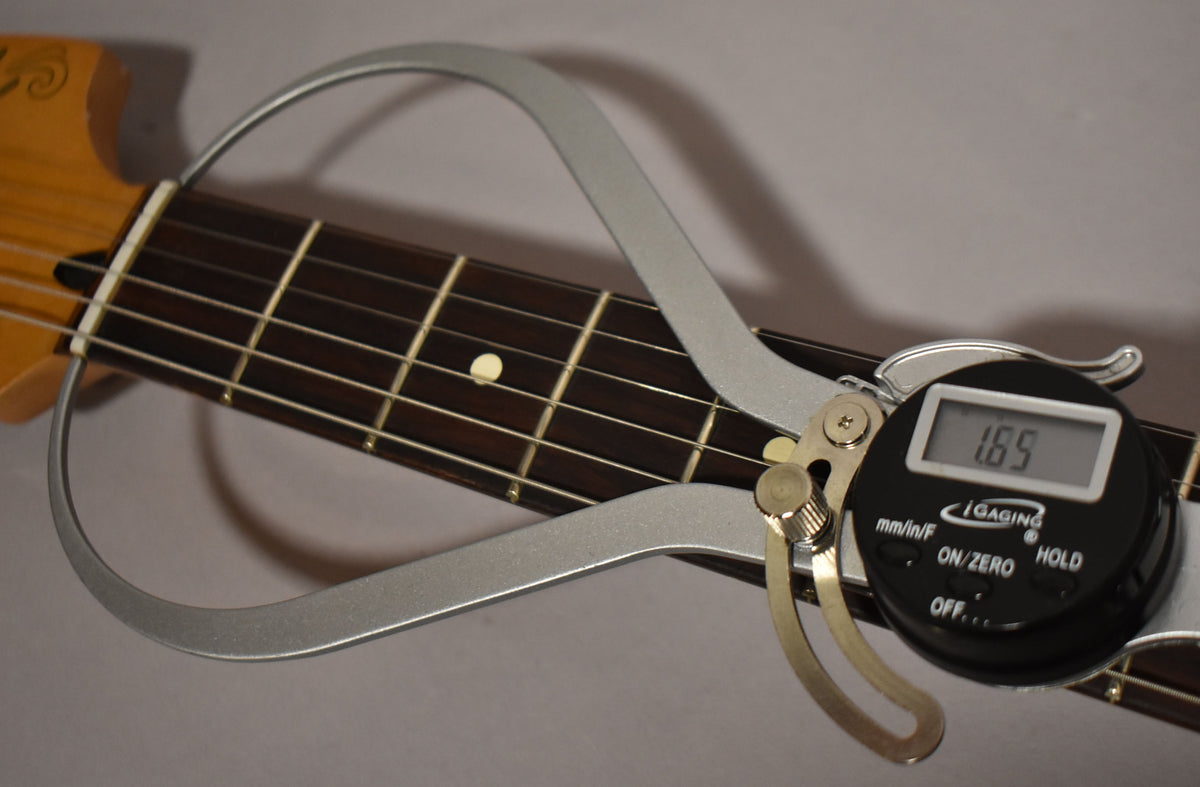 A close-up of the guitar's dark fretboard and light frets, with a digital fret rocker showing a reading of 1.65.