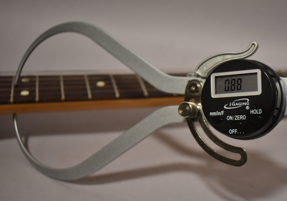 Close-up of a digital caliper measuring the fret height on a dark rosewood fretboard with cream dot inlays.
