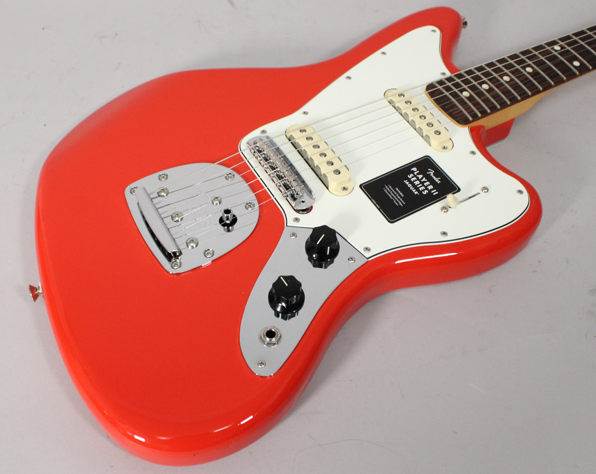 The coral red Jaguar electric guitar is angled from the lower bout, showing its vibrato, bridge, two cream pickups, and controls.