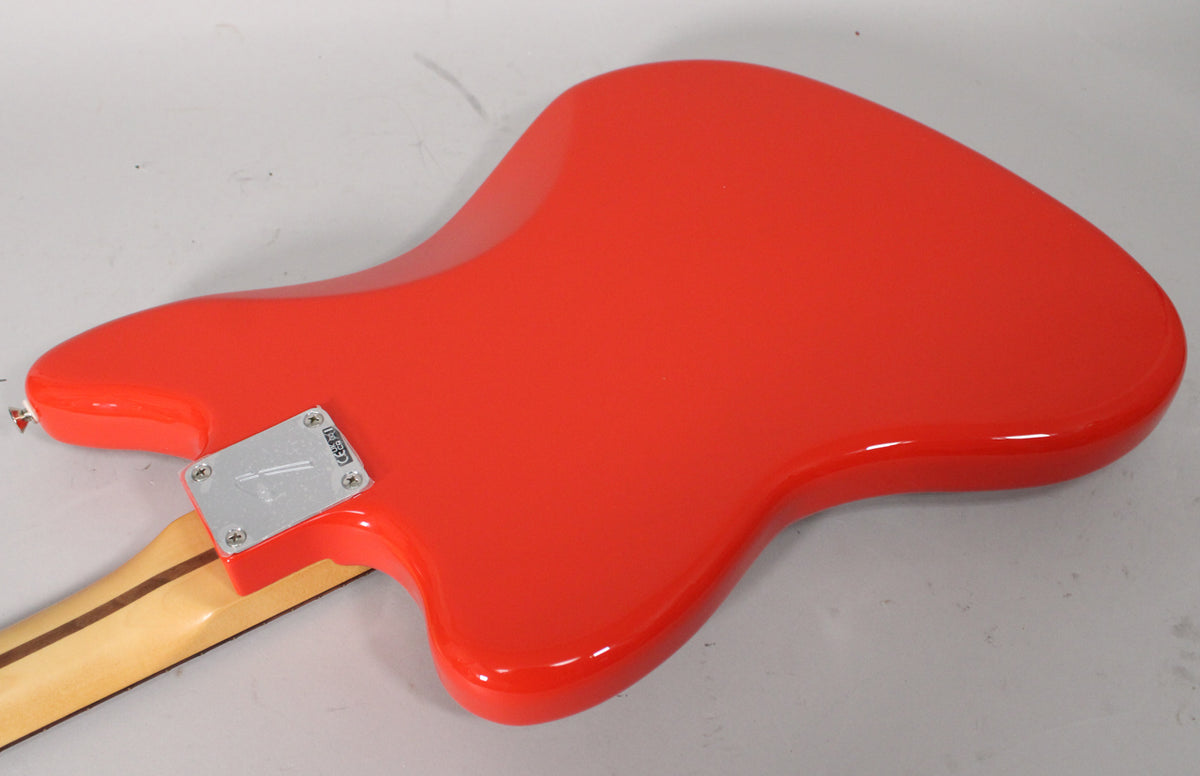 The back of a glossy coral red Jaguar guitar, angled from the neck joint, showing the chrome neck plate and maple neck.