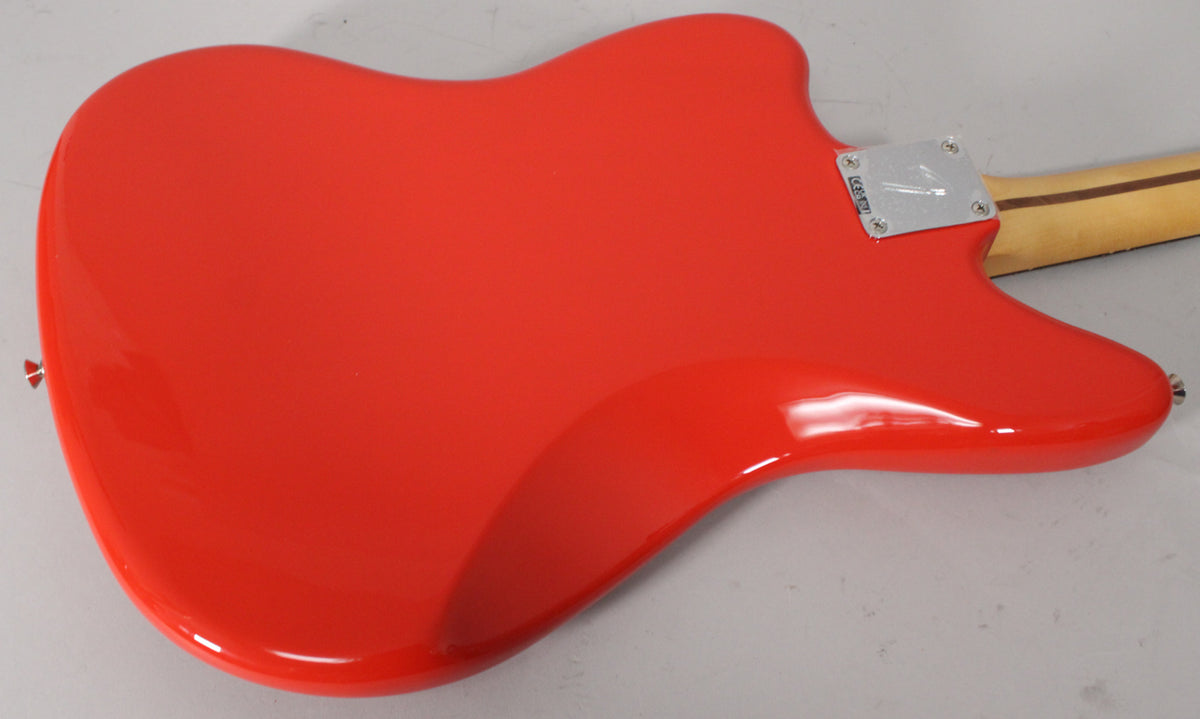 The glossy coral red Jaguar body is seen from the back, with a chrome neck plate and a light wood neck extending to the right.
