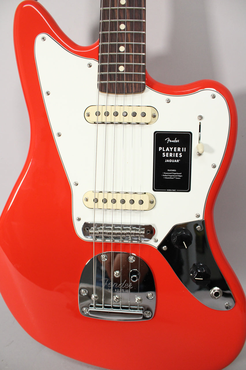 Close-up of a glossy coral red Jaguar electric guitar with a white pickguard, two cream single-coil pickups, and chrome hardware.