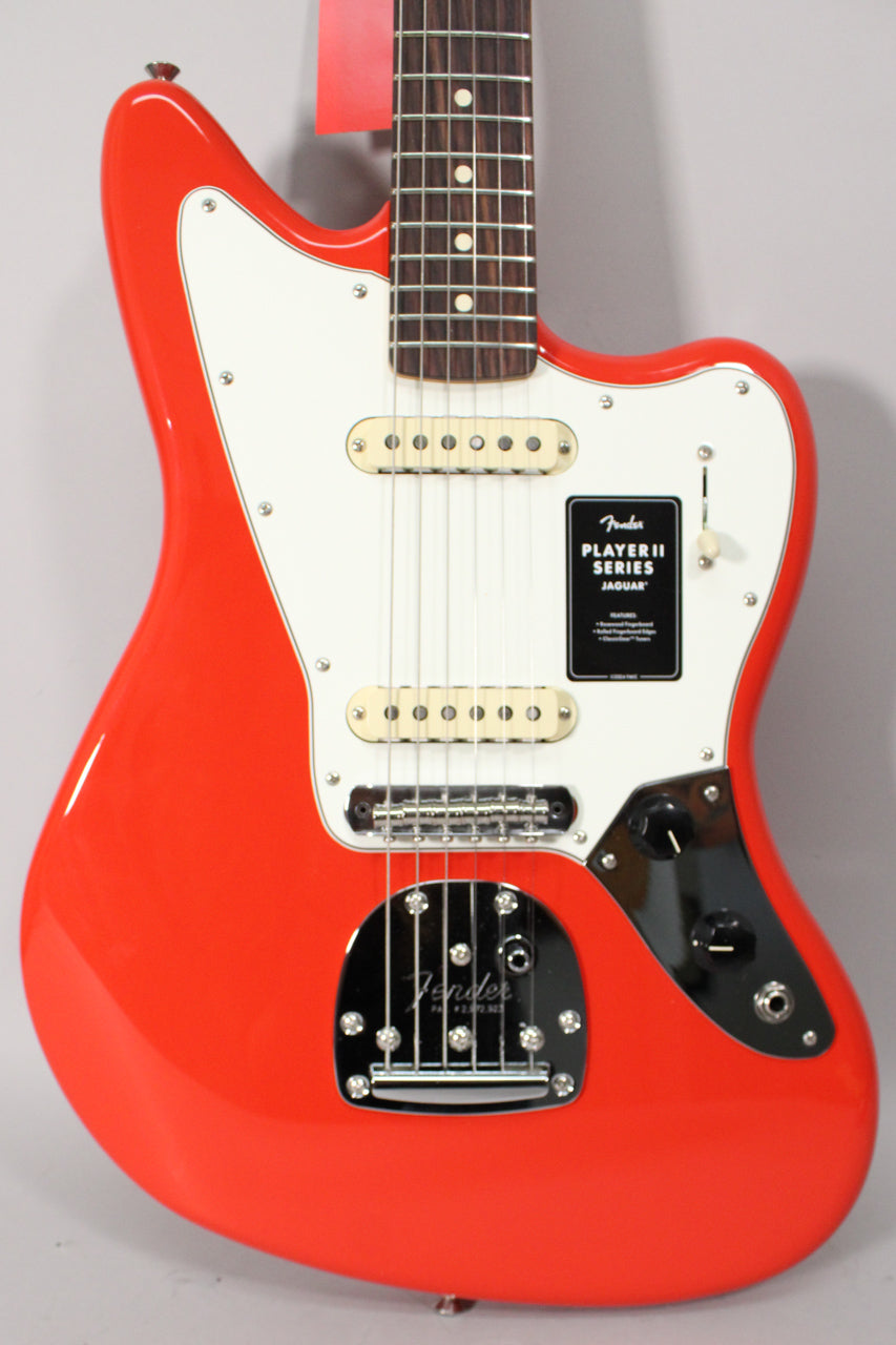A coral red Jaguar electric guitar, angled slightly right, showing its white pickguard, two single-coil pickups, and chrome vibrato system.