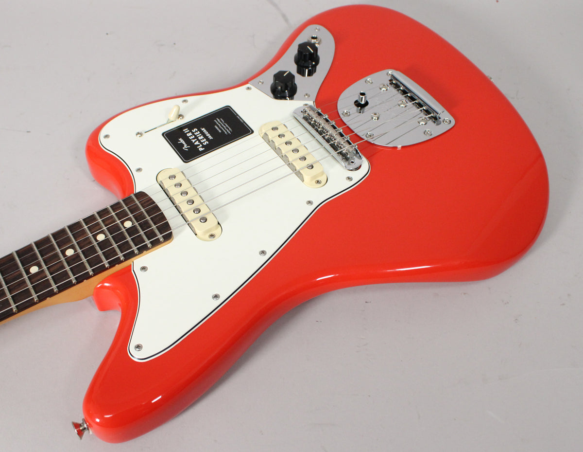 Coral Red Jaguar electric guitar, angled view of the body and lower neck, with a white pickguard, two cream pickups, and chrome hardware.