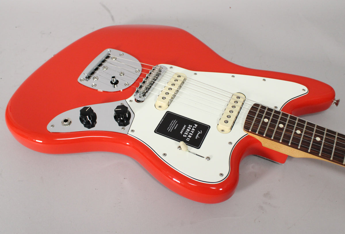 Coral Red Jaguar, angled from above, showing the glossy body, white pickguard, chrome hardware, and rosewood fretboard.