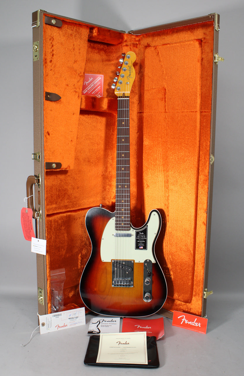 Full view of a 3-color sunburst Telecaster with a white pickguard, rosewood fretboard, and chrome hardware, resting in its open brown hardshell case with orange plush lining.