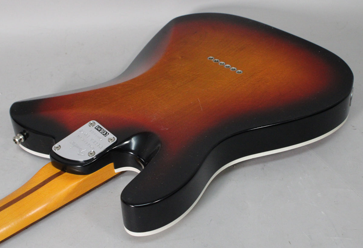 The guitar's back, in 3-color sunburst with white binding, shows six string-through-body ferrules and a chrome neck plate.