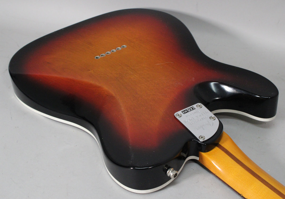 Rear view of a 3-color sunburst Telecaster body with white binding, showing the neck plate, output jack, and six string-through-body ferrules.