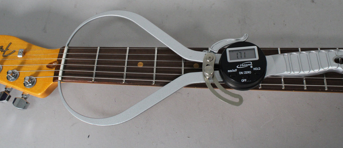 A digital caliper measures the nut width of the guitar's dark fretboard, showing "1.71" on its display.