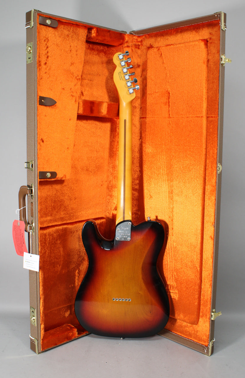 The Telecaster's 3-color sunburst back and maple neck are visible, standing upright in its open brown hard case with orange plush lining.