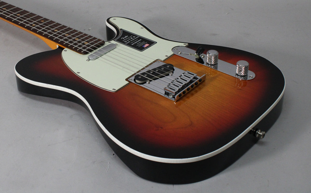 The Telecaster's 3-color sunburst body is angled, showing the chrome bridge, knurled control knobs, and cream pickguard.