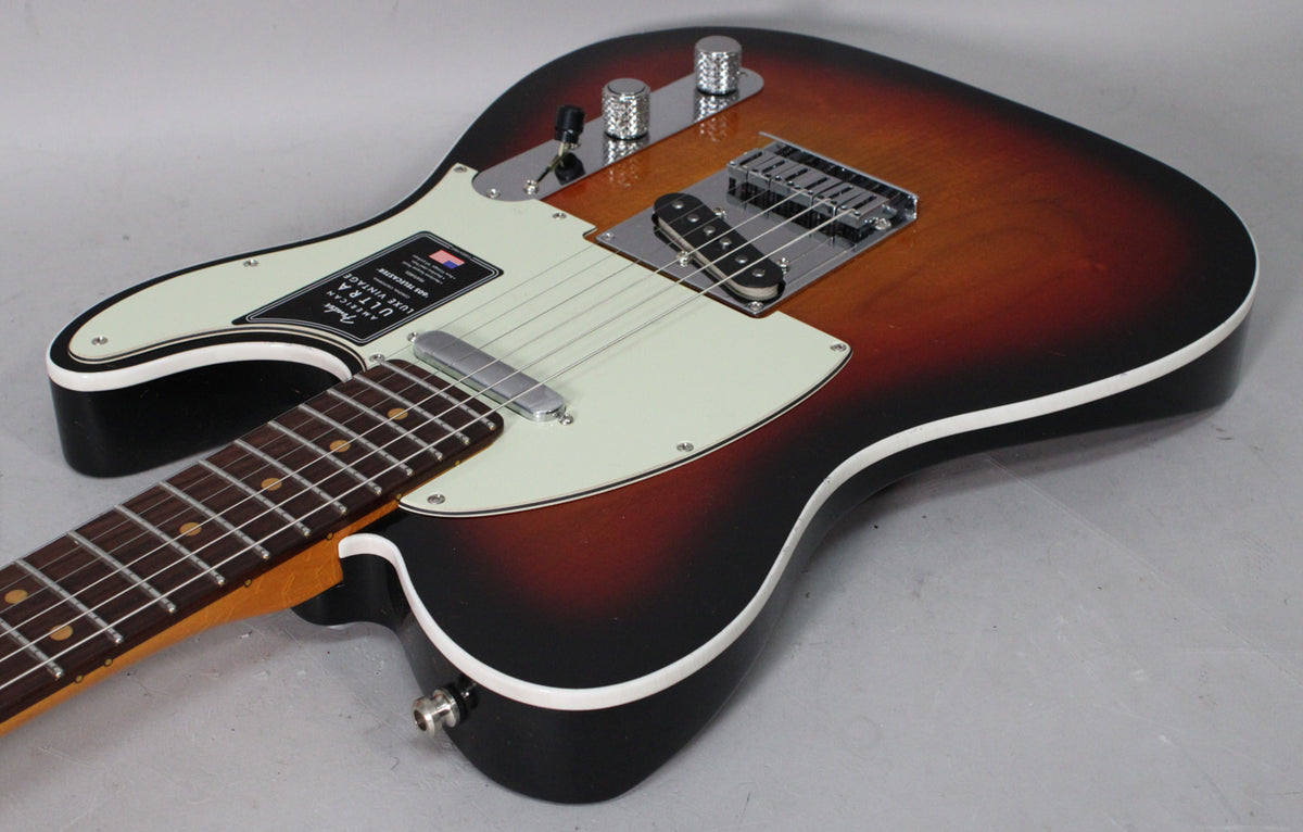 The Telecaster's sunburst body, with white binding, is angled from the neck to the lower bout, showing a cream pickguard and chrome hardware.