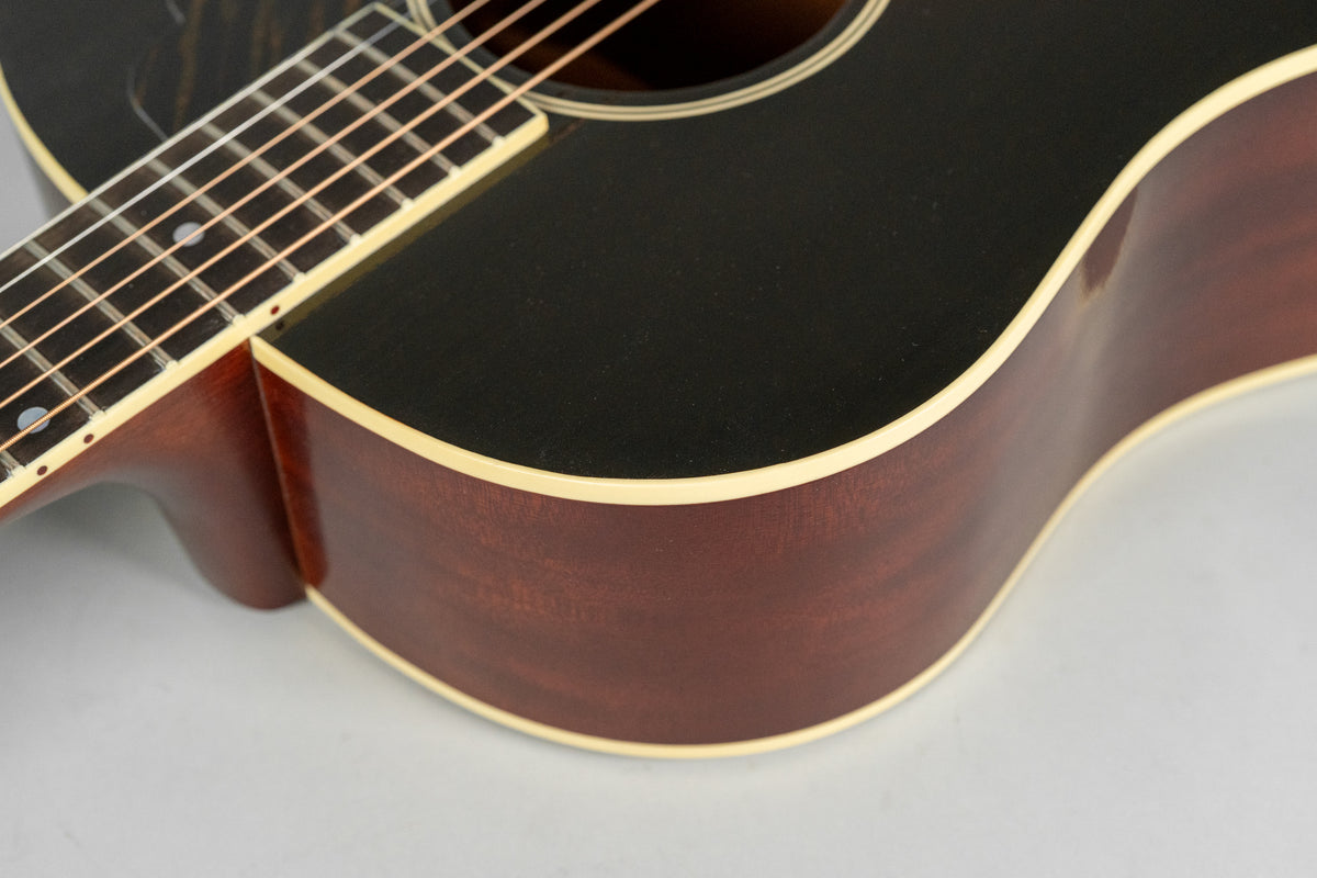 Close-up of the guitar's upper bout, showing the black top, dark reddish-brown sides, and cream binding with light checking.