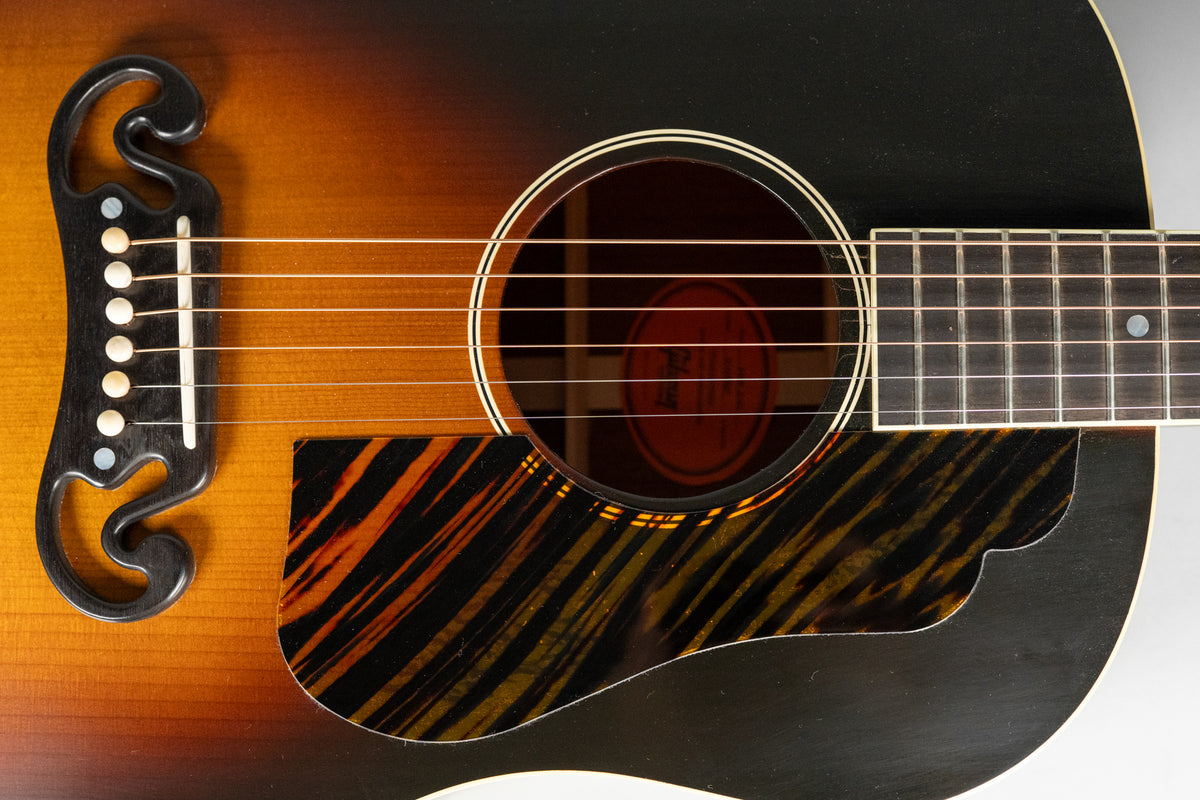 Close-up of the guitar's sunburst body, soundhole, and tiger-stripe pickguard, showing the bridge and lower fretboard.