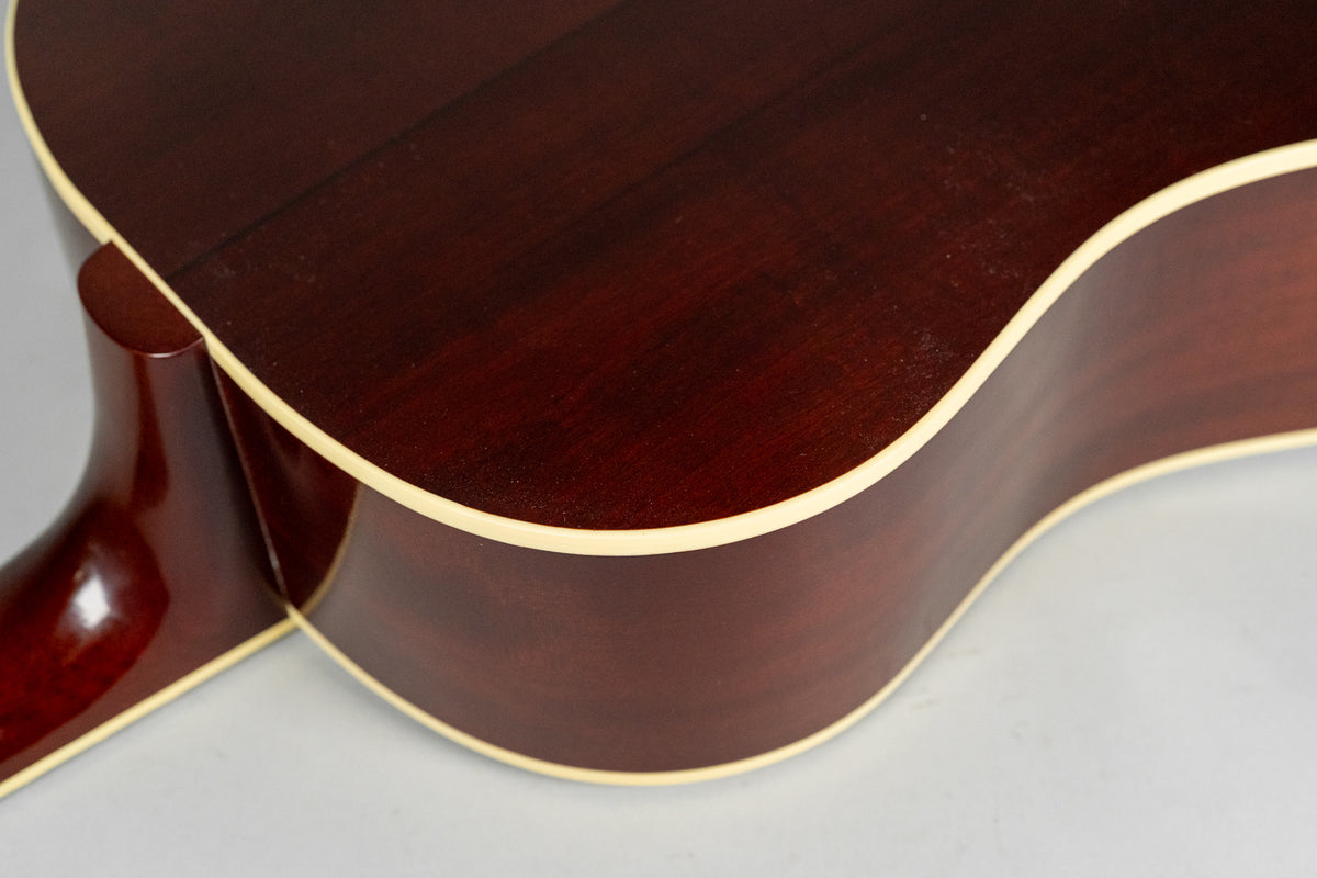The dark brown acoustic guitar's lower bout and neck heel are visible, with cream binding along the body's edge.