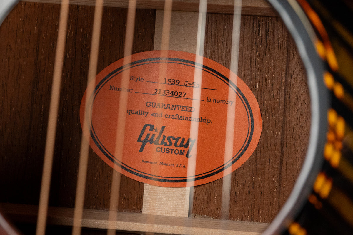 A close-up of the guitar's interior, showing an orange oval label with black text and the internal bracing of the dark wood body.