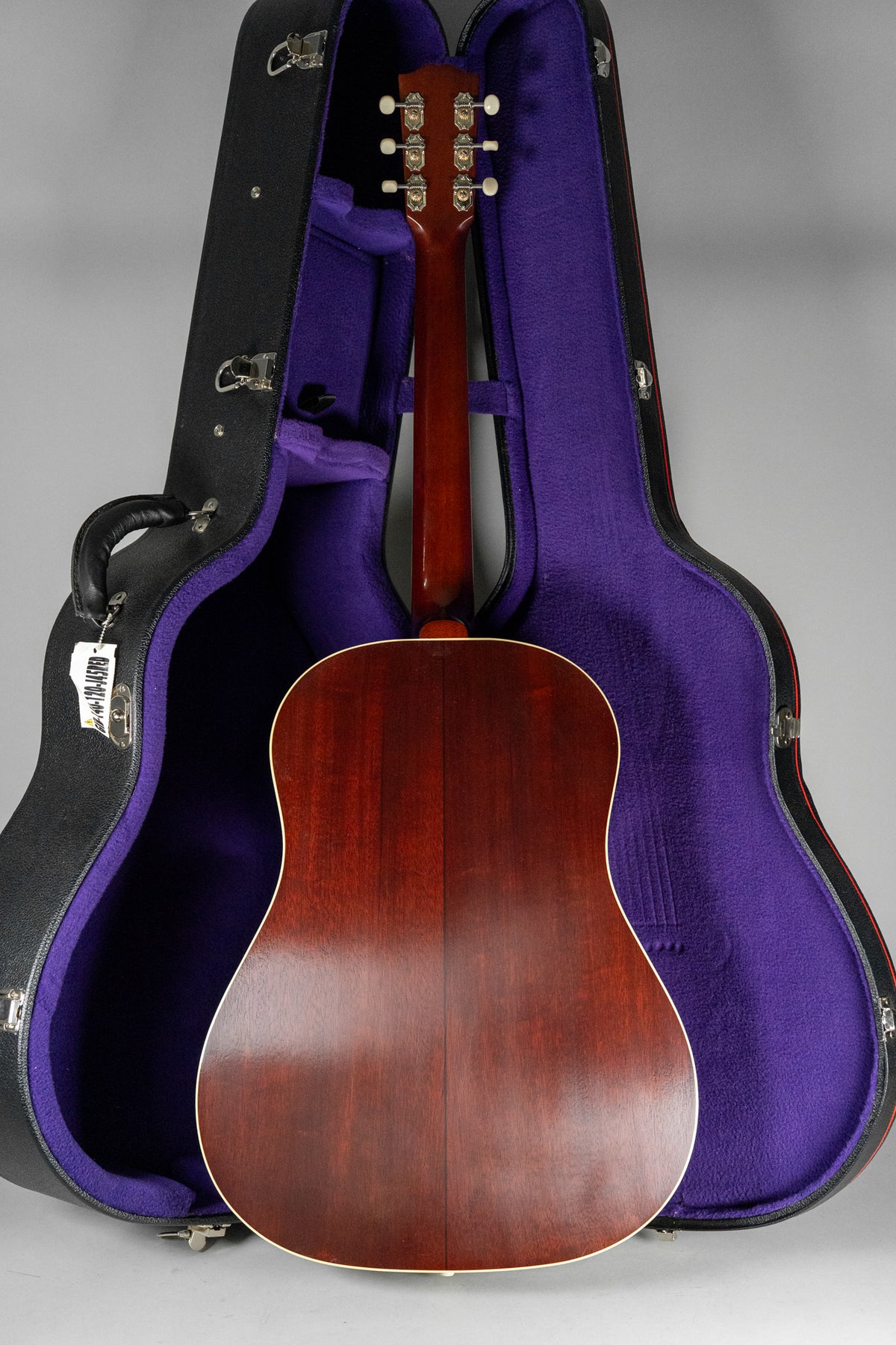 The acoustic guitar's dark reddish-brown back and neck are visible, standing in a black open case with a vibrant purple interior.