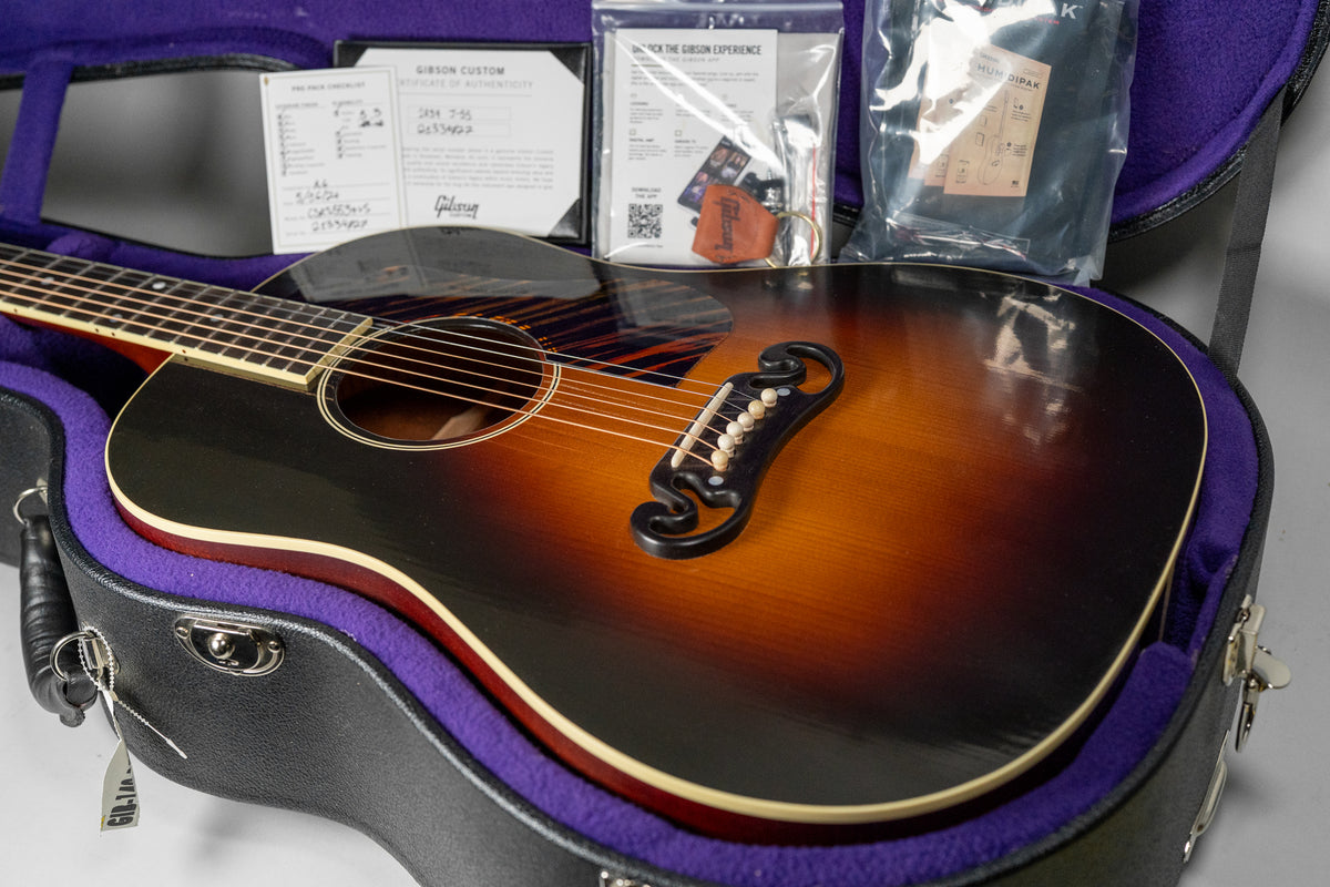 The guitar's sunburst body, with a dark upper bout and lighter lower bout, is nestled in a purple-lined case with paperwork.