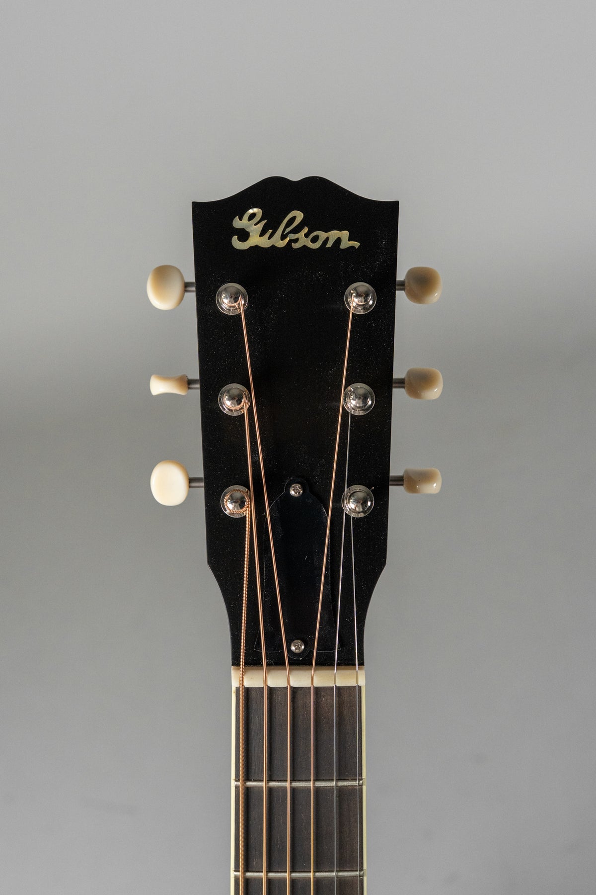 The guitar's black headstock with a mother-of-pearl inlay and six cream-colored tuning pegs is centered, showing the top of the fretboard.
