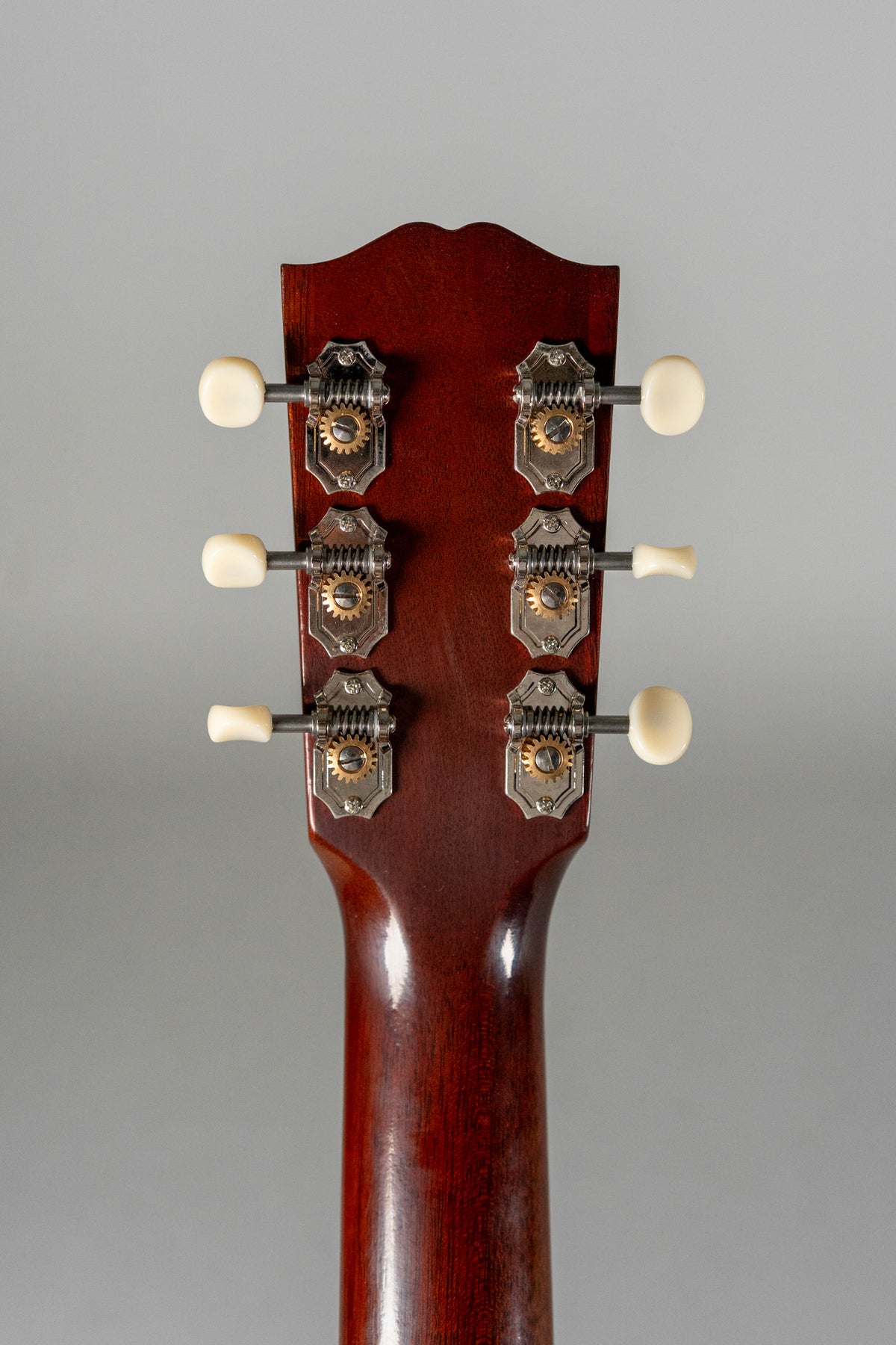 The guitar's dark brown headstock and neck, with six open-gear tuners featuring cream buttons, are viewed from the rear.