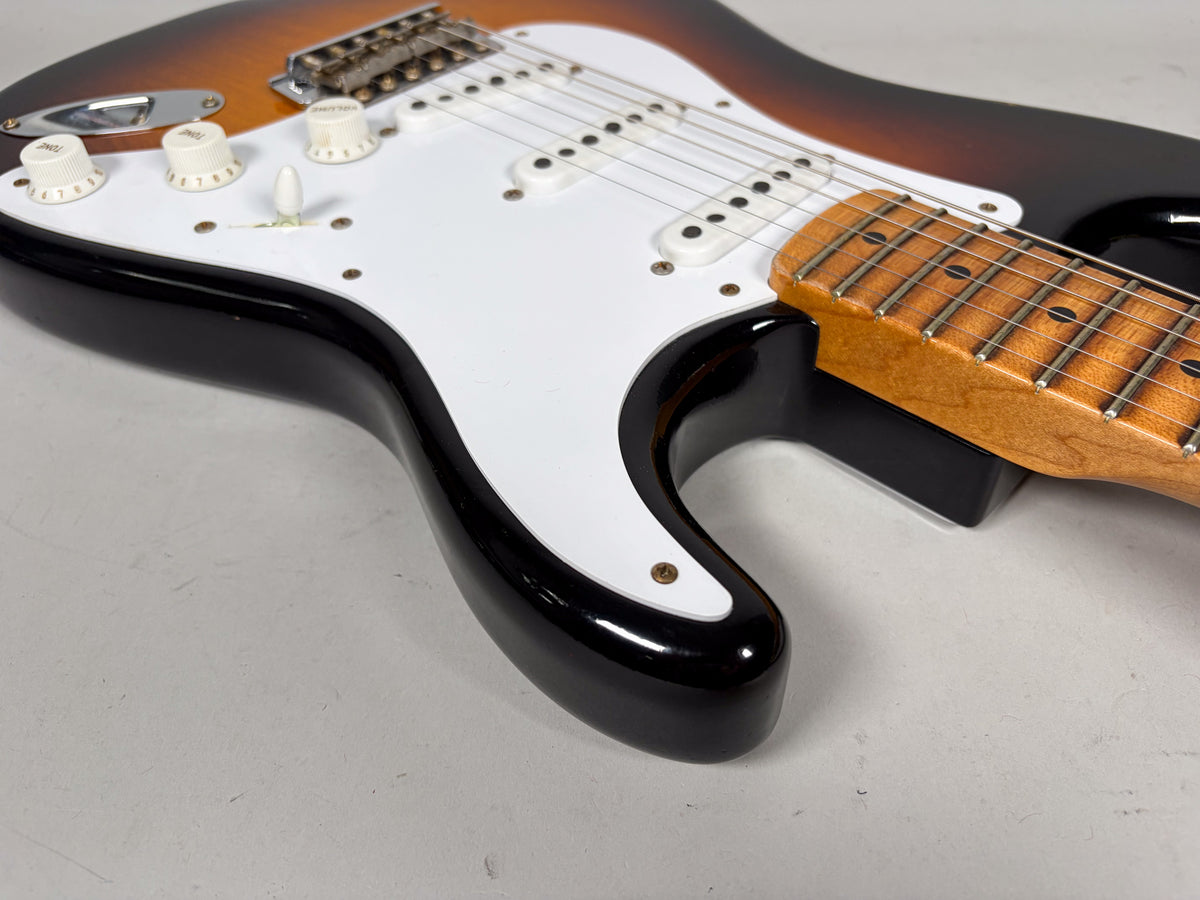 Upper body of a sunburst Stratocaster, showing the white pickguard, three cream knobs, pickup selector, and maple fretboard.