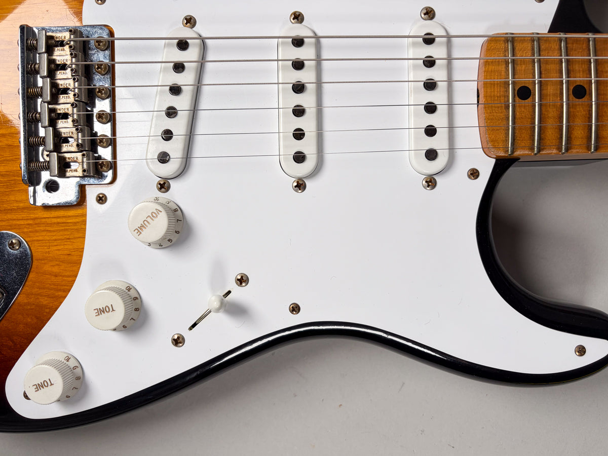Close-up of the guitar's lower body, showing a white pickguard, three single-coil pickups, three cream control knobs, and a 5-way switch.