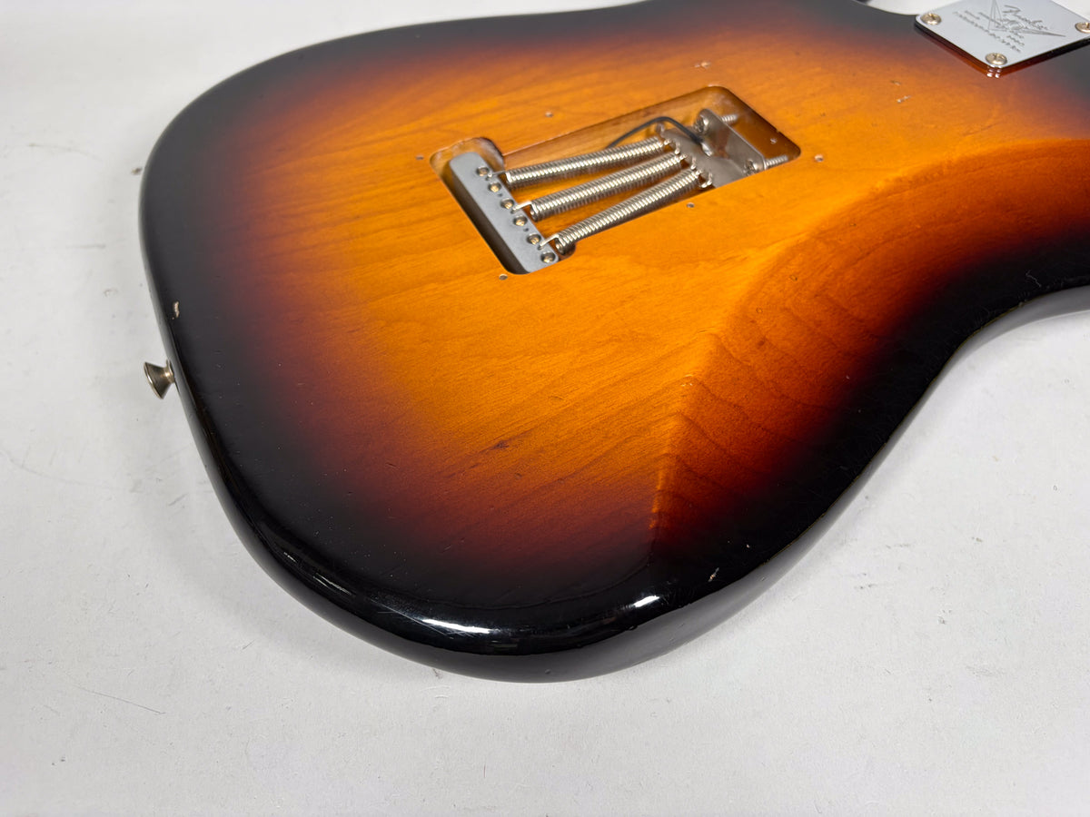 The back of the sunburst guitar body shows the tremolo spring cavity, a neck plate, and light relic wear on the finish.