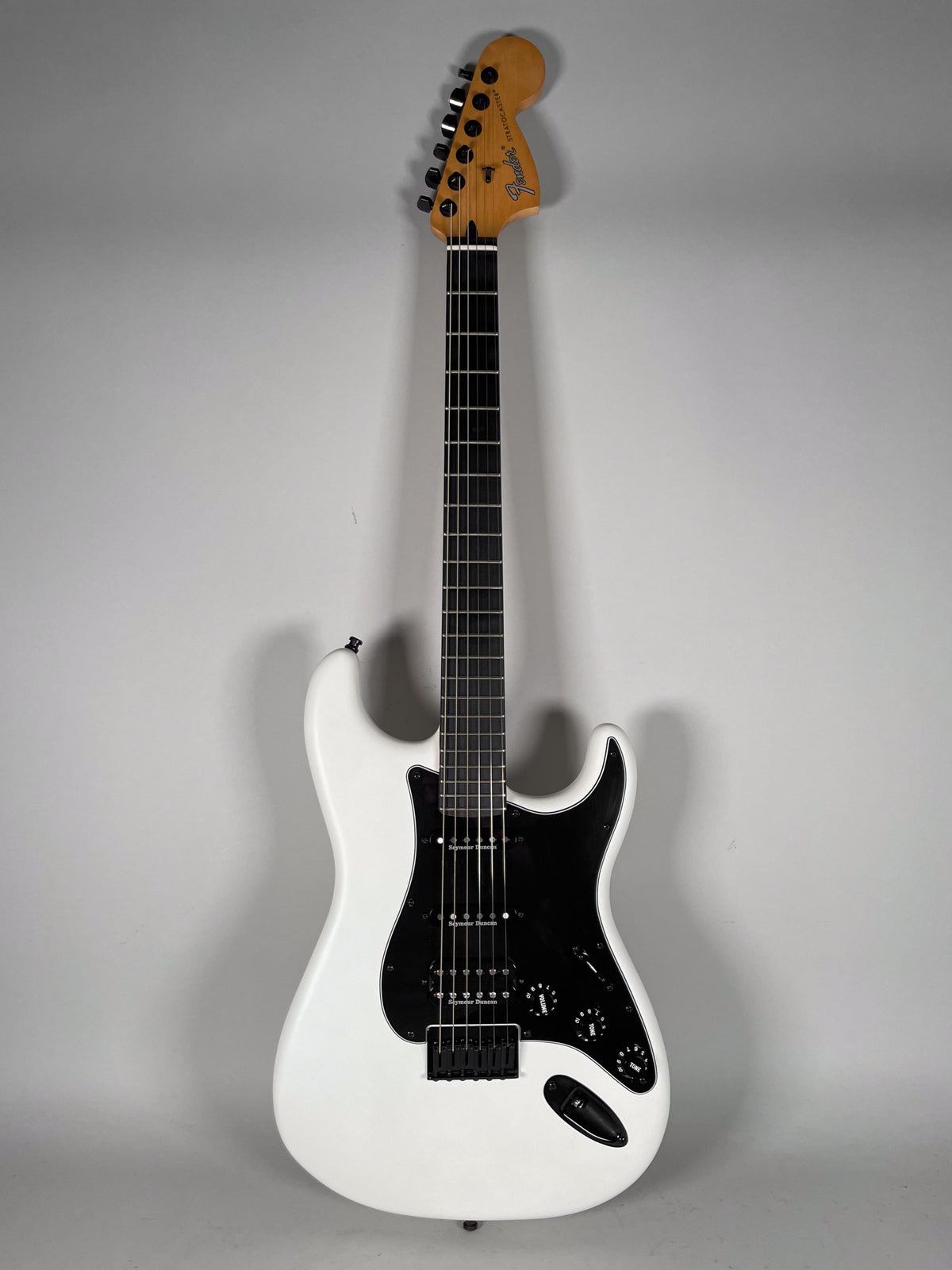 Full-length view of a white Stratocaster with a black pickguard, black humbucker and two single-coil pickups, and black hardware.
