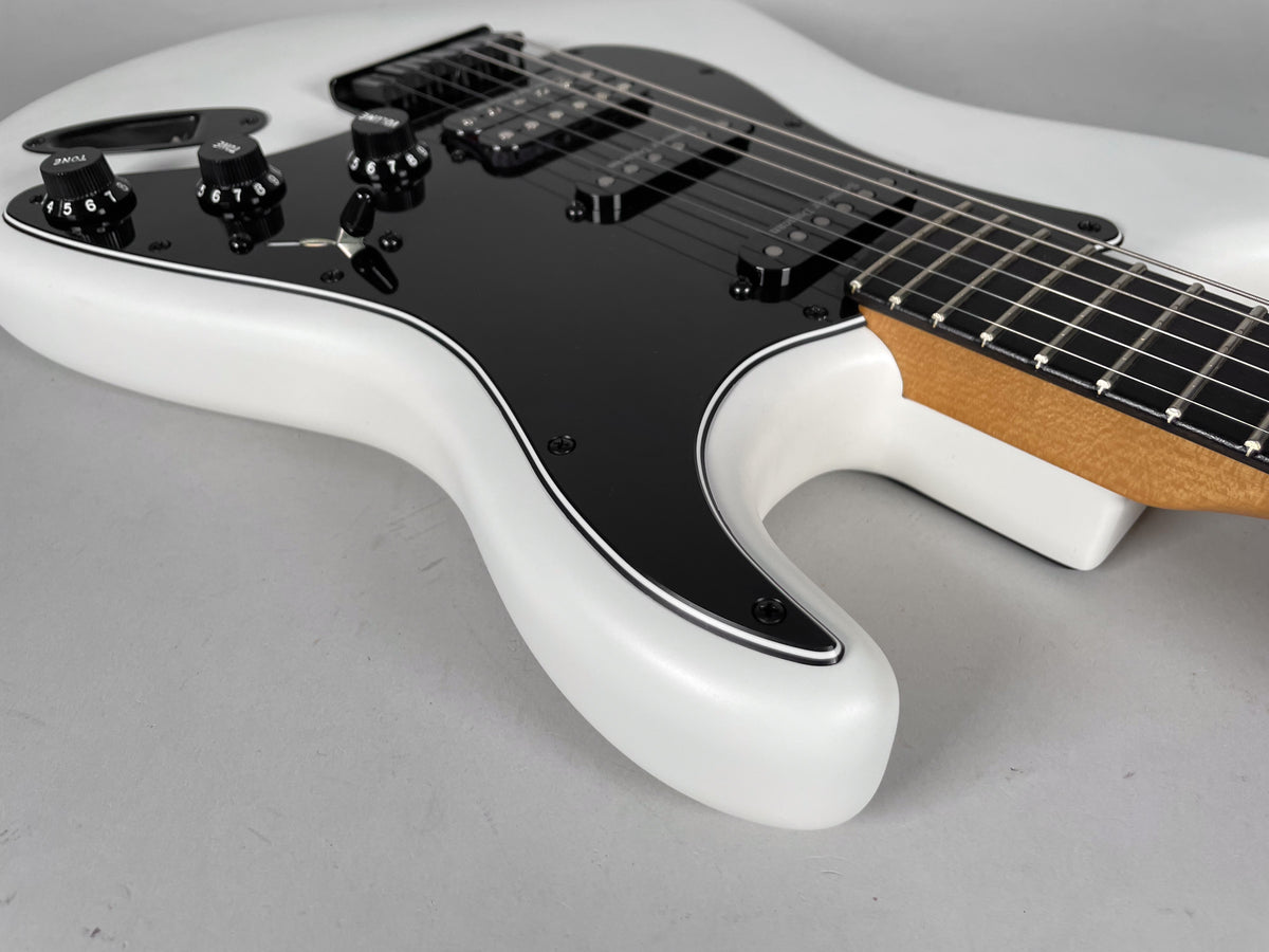 The white Stratocaster body, with a black pickguard and black HSS pickups, is angled from the lower bout towards the headstock.