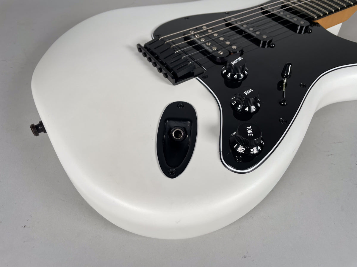 Close-up of a white electric guitar body with a black pickguard, showing the output jack, three black control knobs, and a 5-way switch.