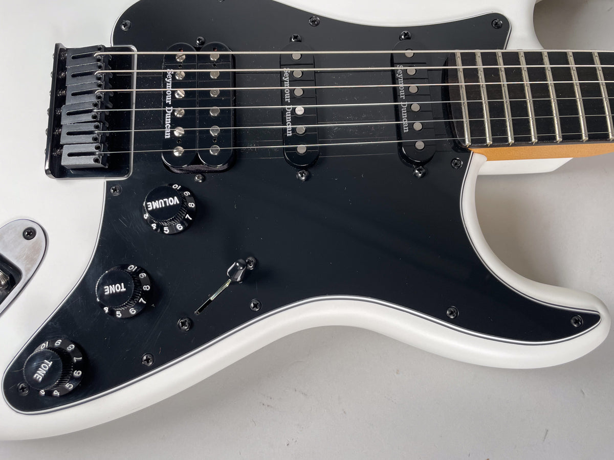 Upper body of a white Stratocaster with a black pickguard, HSS pickups, black hardtail bridge, and three black control knobs.