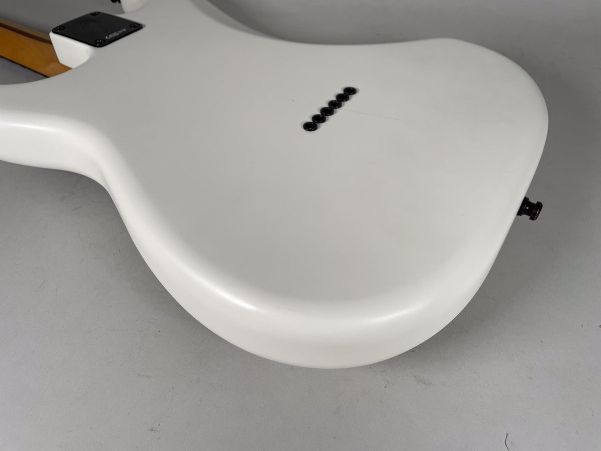 The back of a white hardtail electric guitar, showing six black string ferrules and a black output jack.