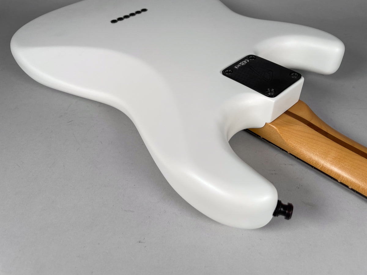 The guitar's matte white body, viewed from the back, shows a black neck plate, six string ferrules, and a black output jack.