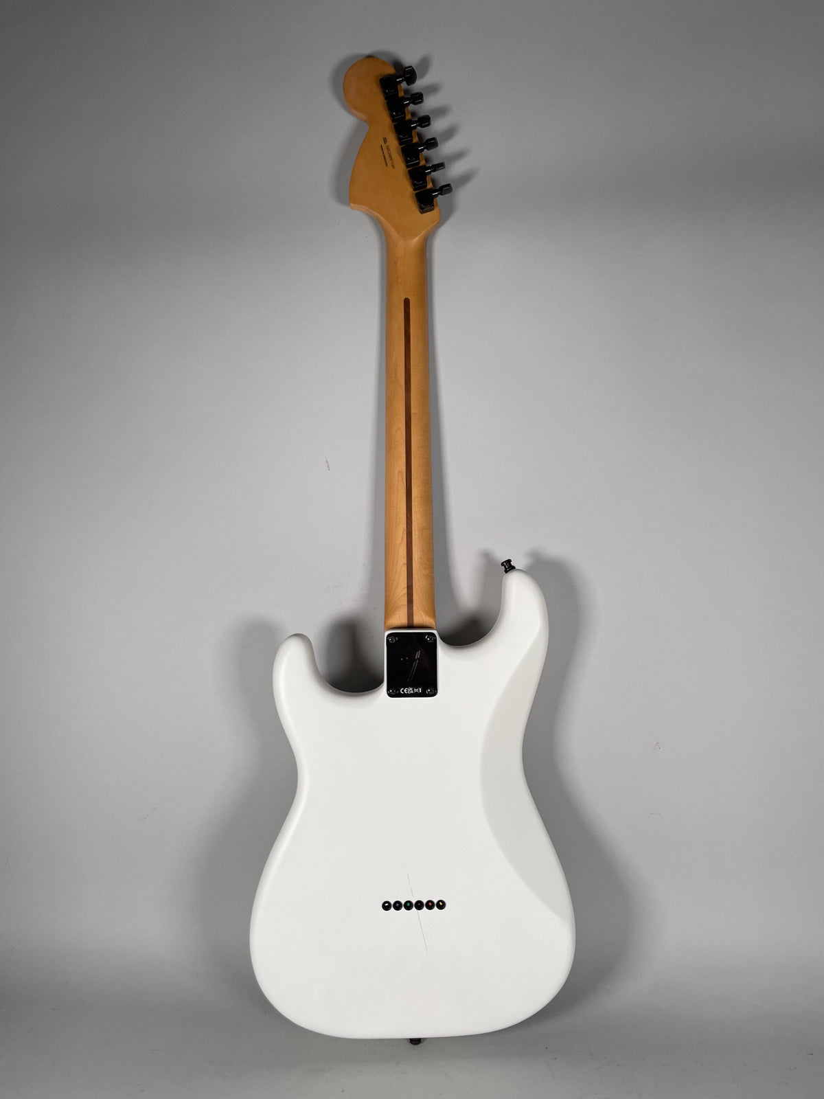 Full rear view of a white Stratocaster with a maple neck, black tuners, and six string-through-body ferrules.