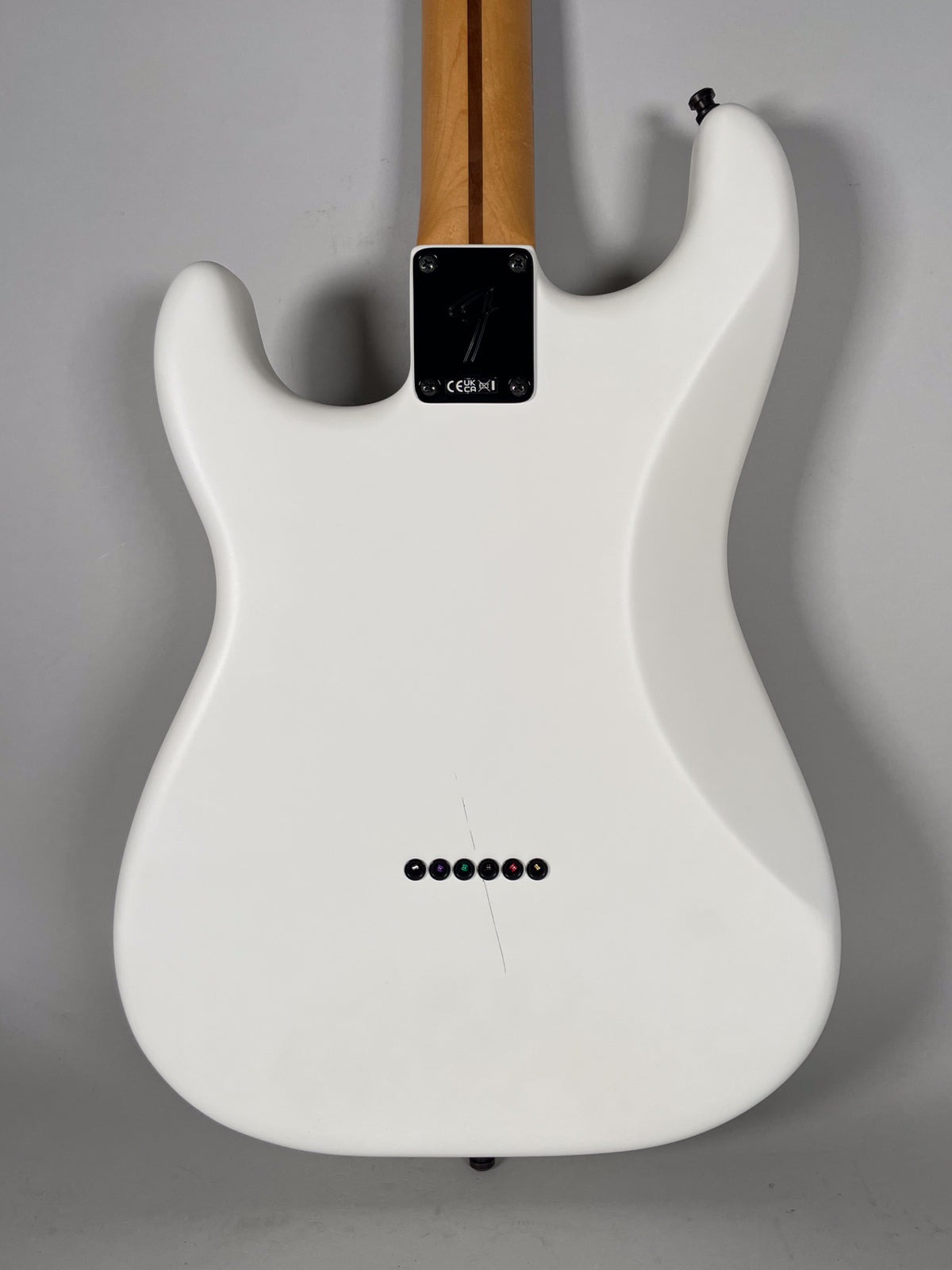 The back of a white Stratocaster body with a maple neck, showing six string-through-body ferrules and a fine scratch.