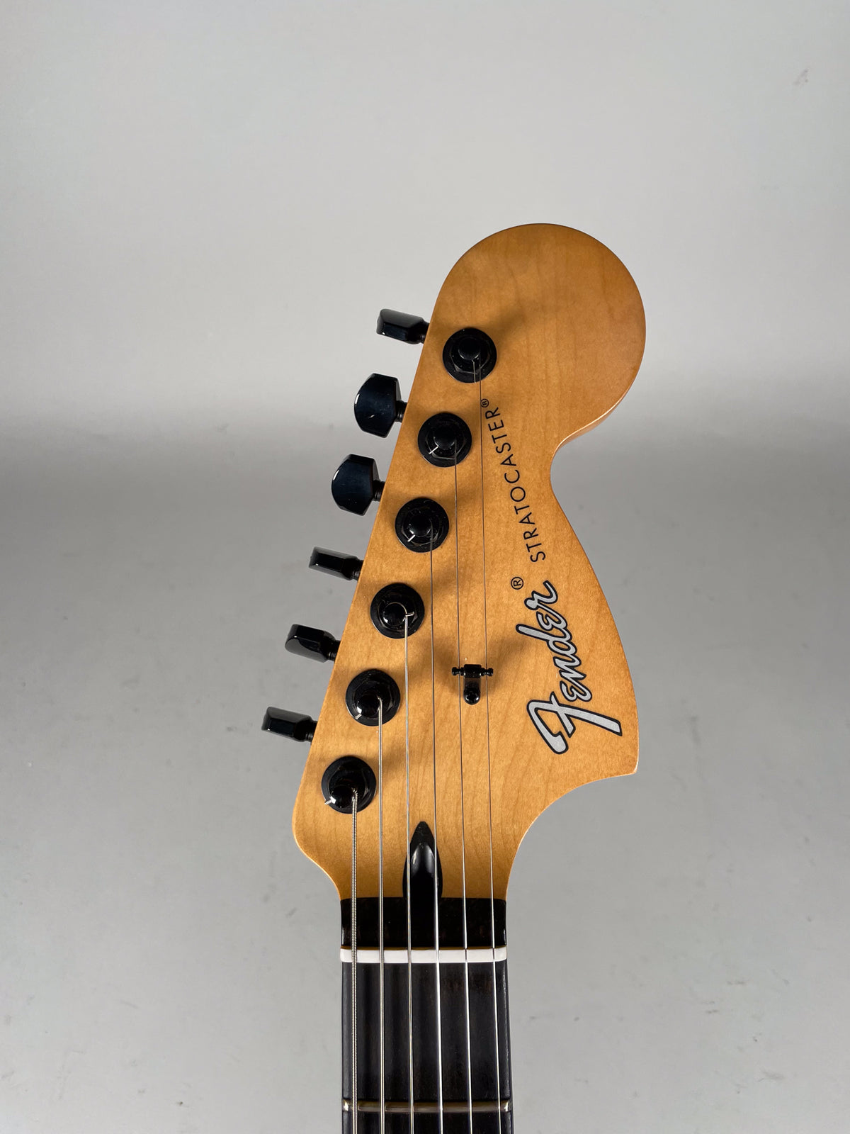 Close-up of the light-colored maple headstock with black tuning pegs and string tree, angled slightly right, showing the top half.