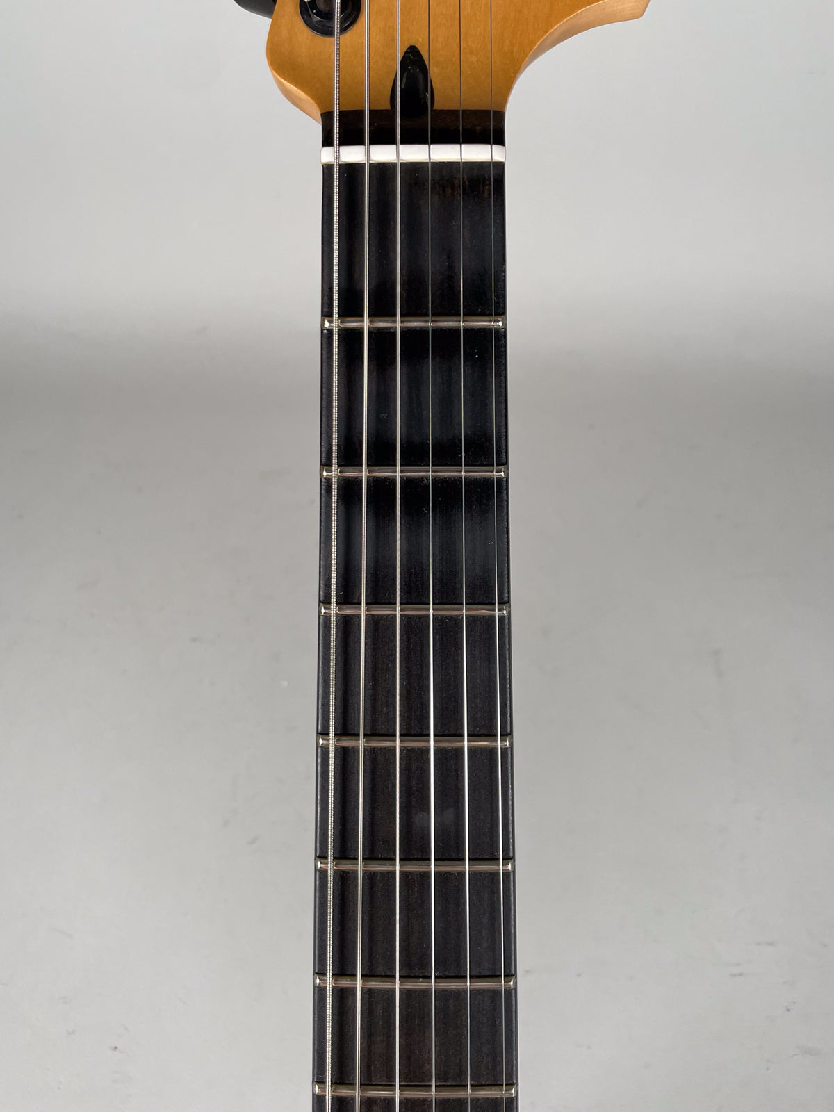 The guitar's dark fretboard and light maple neck are viewed from above, showing the nut and first 10 frets.