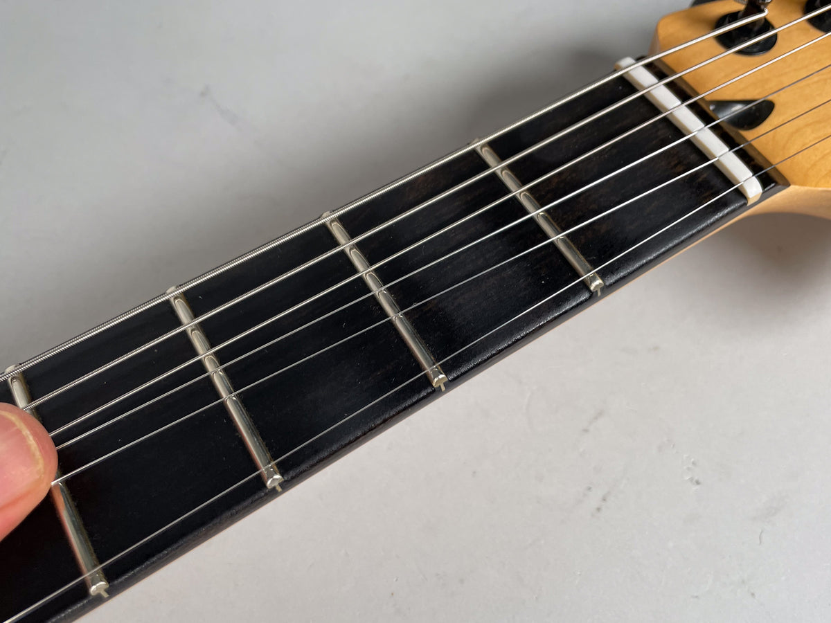 Close-up of the dark fretboard and silver frets, with a white nut and light wood headstock visible at the top right.